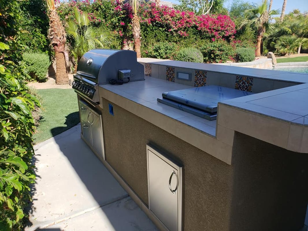 Long custom grill island beside a lush garden and swimming pool