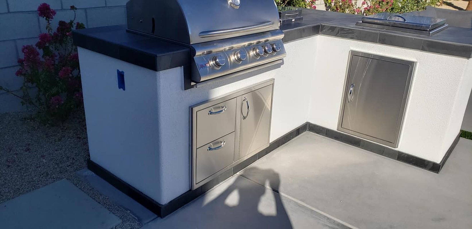 White stucco L-shaped outdoor kitchen with stainless grill and storage